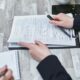 Free Close-up of hands analyzing insurance policy paperwork with pen on table. Stock Photo